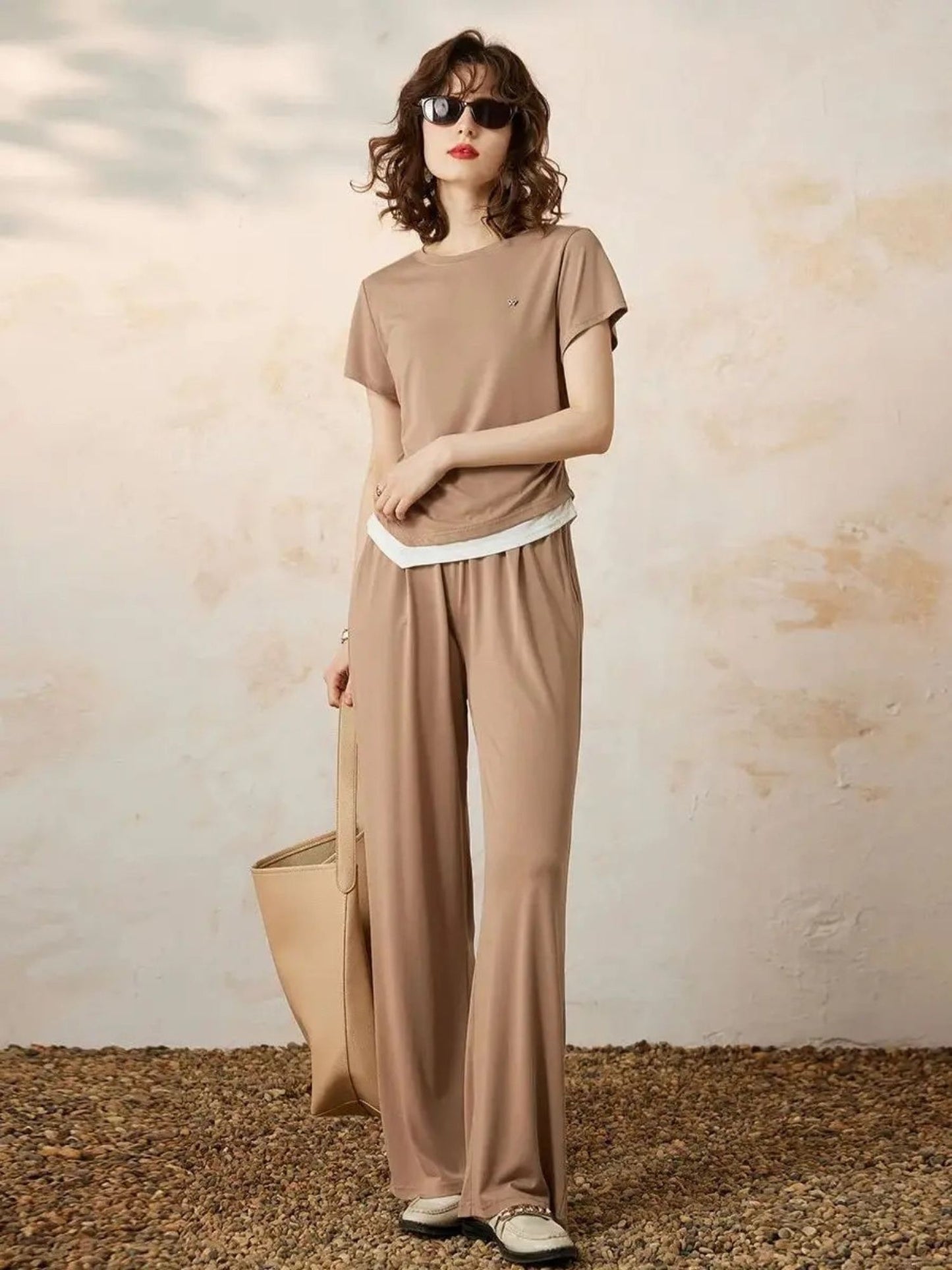 Modell smilende i beige sett med runde solbriller og flate sko