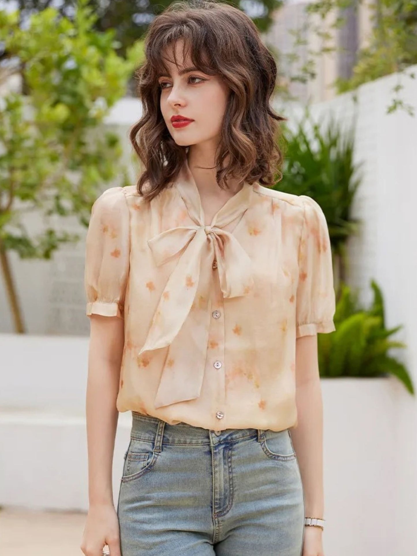 Modell i lys oransje bluse med print og blå jeans, smilende