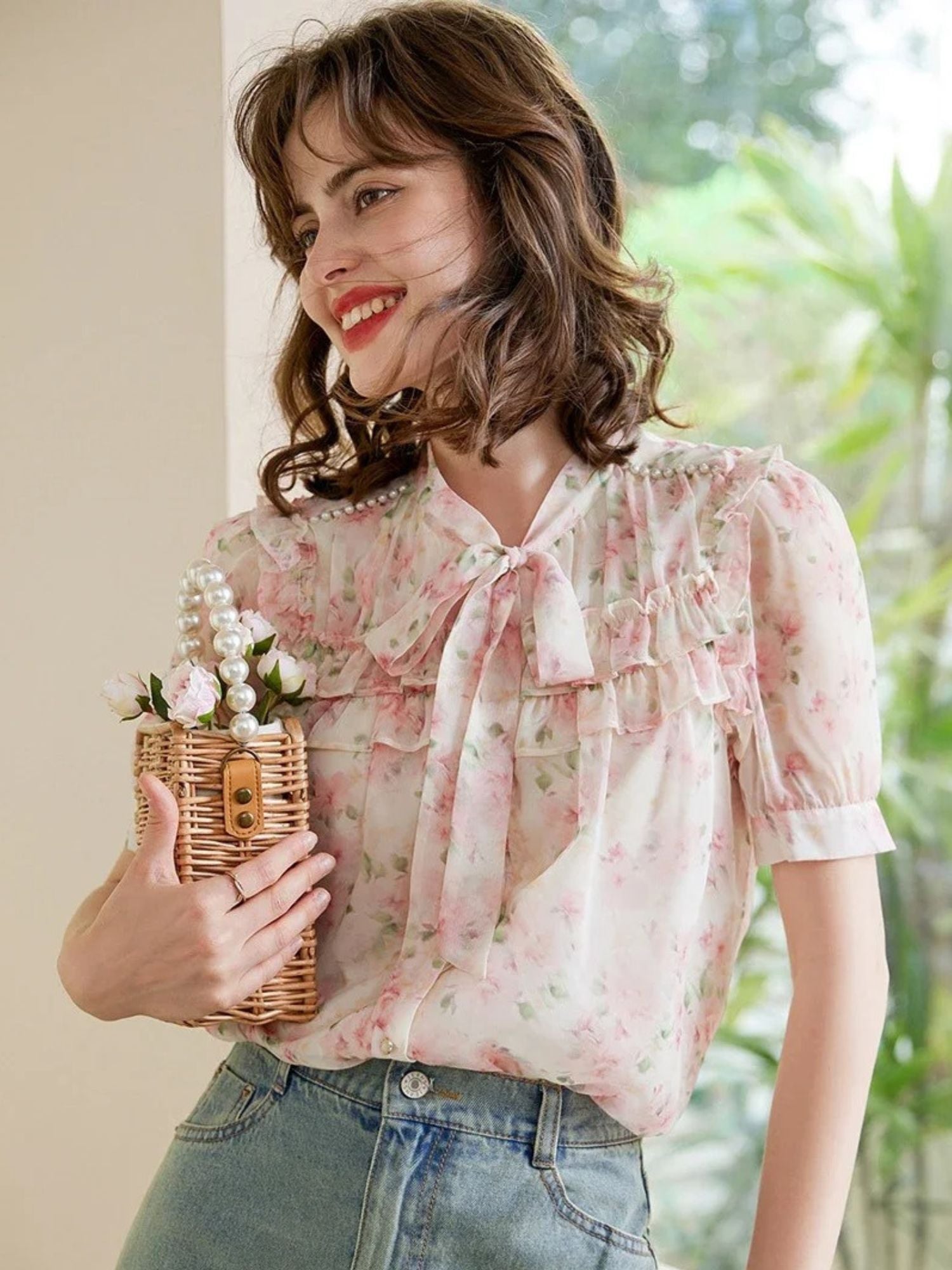 Modell smilende i rosa blomstrete bluse med sløyfe og lyseblå jeans
