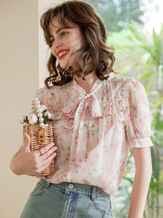 Modell smilende i rosa blomstrete bluse med sløyfe og lyseblå jeans