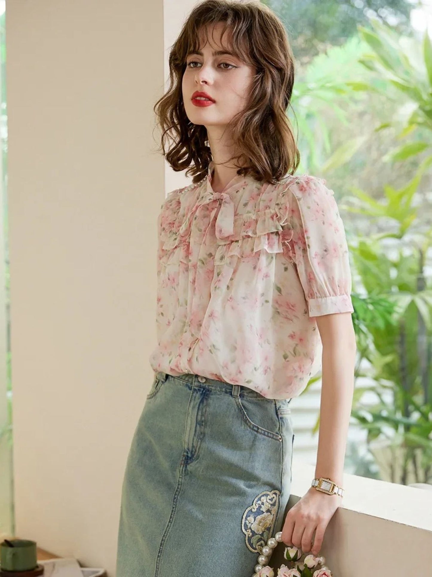 Modell i rosa bluse og denimskjørt, ser til siden