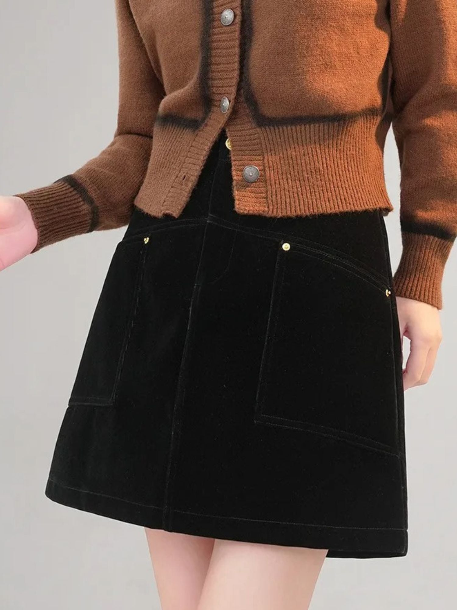 Frontbilde av modell i svart kordfløyelsskjørt med store lommer og brun cardigan