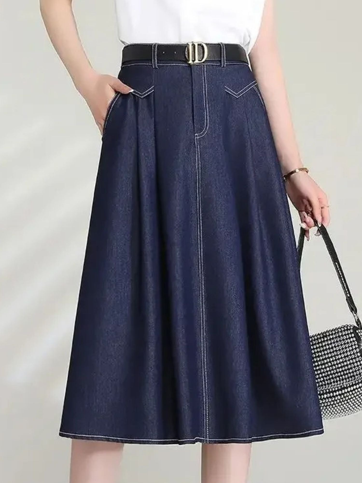 Model wearing high-waisted A-line denim skirt with front pleats and black belt
