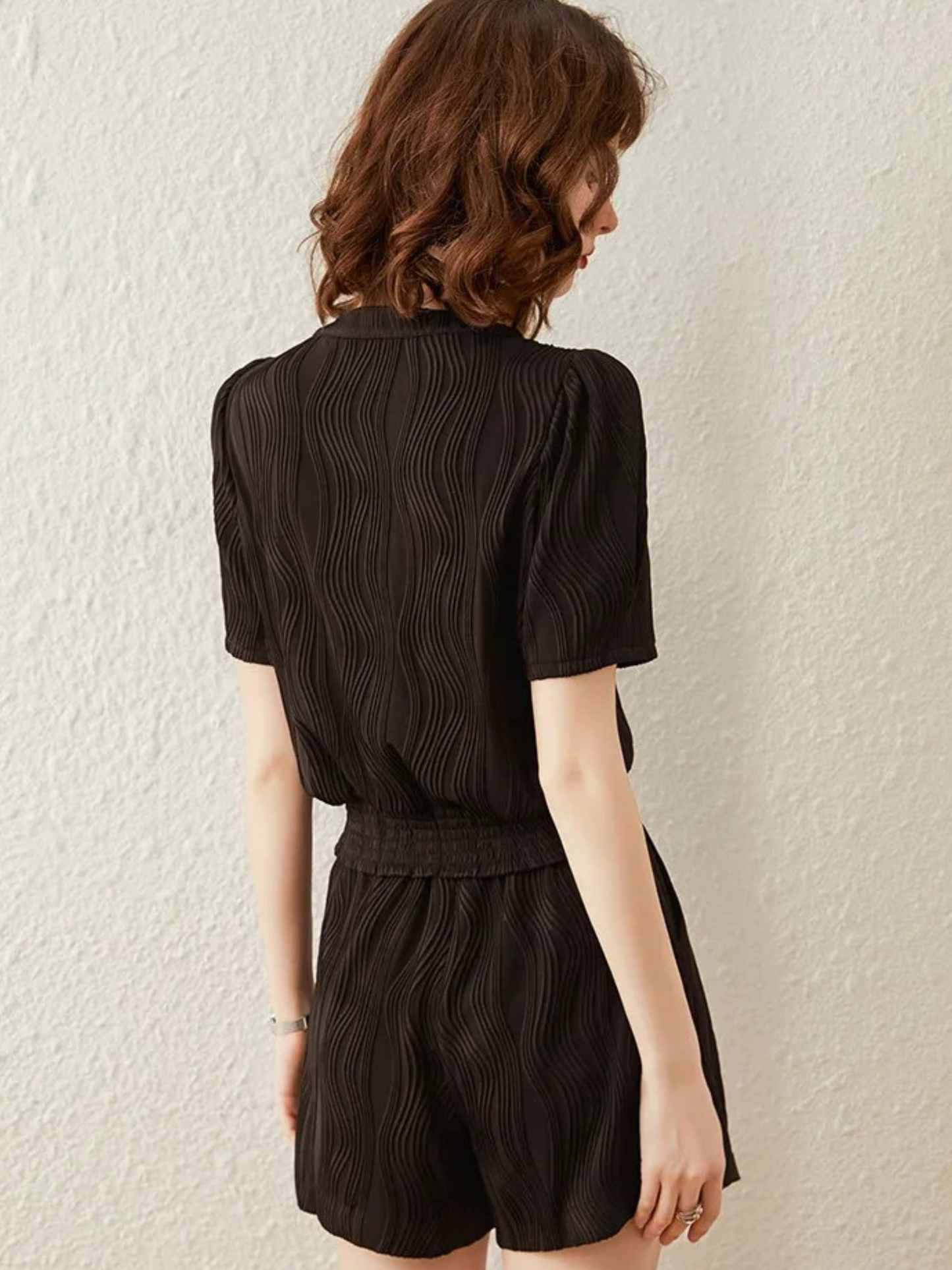 Bakfra bilde av kort svart jumpsuit med strukturert stoff og krage